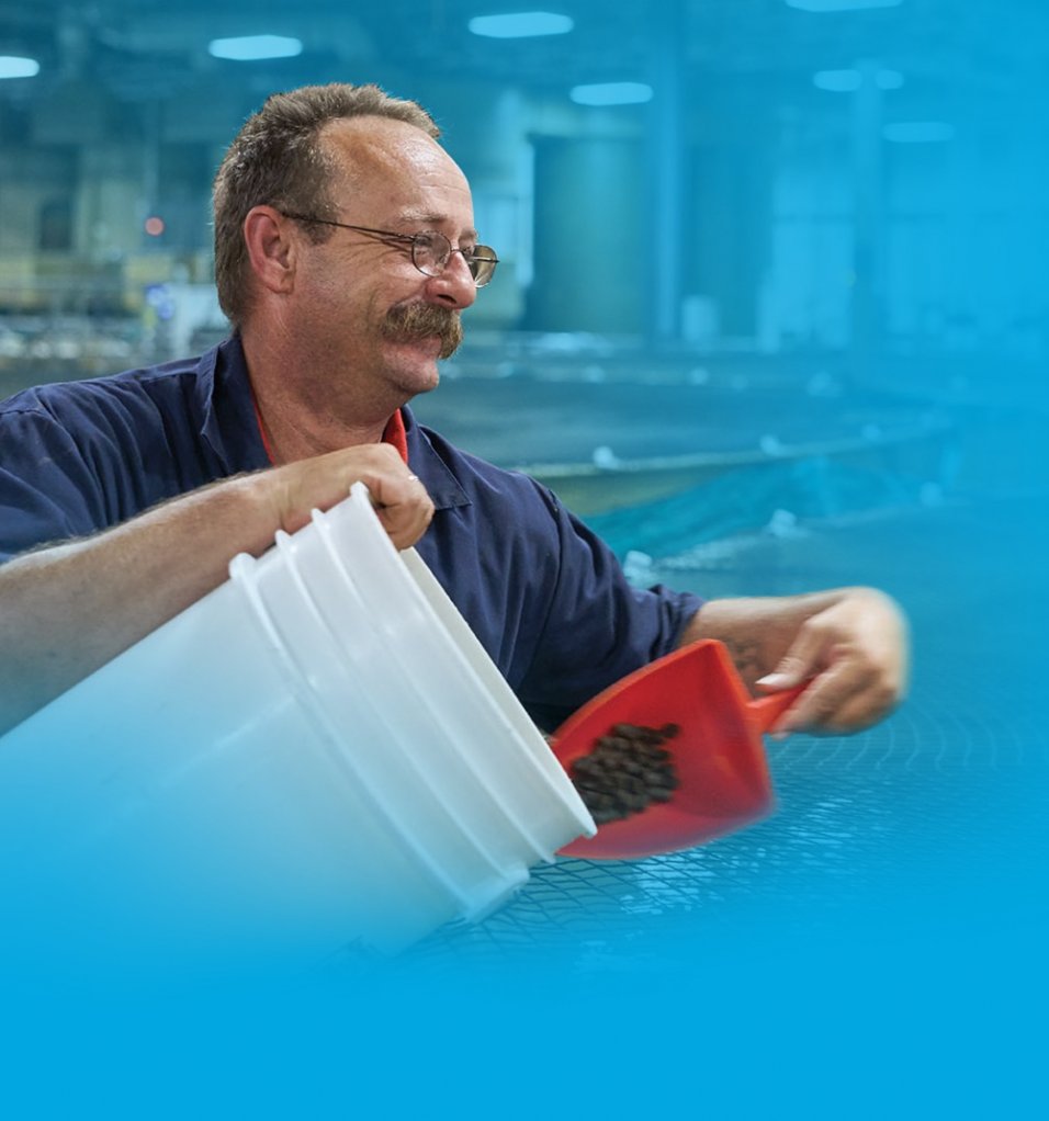 AquaBounty employee smiling and holding white buckets with fish food at the land-based fish farm 